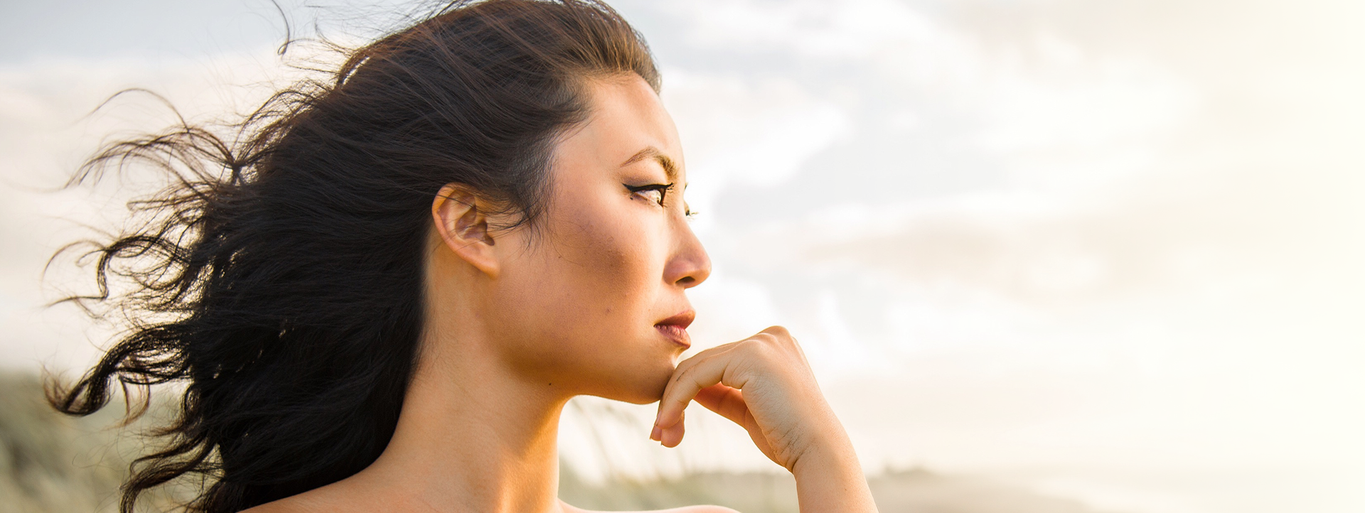 Woman with flowing hair gazing thoughtfully, against a soft, natural background, embodying the elegance and beauty associated with hair services at Envy Studio in Lancaster, PA.