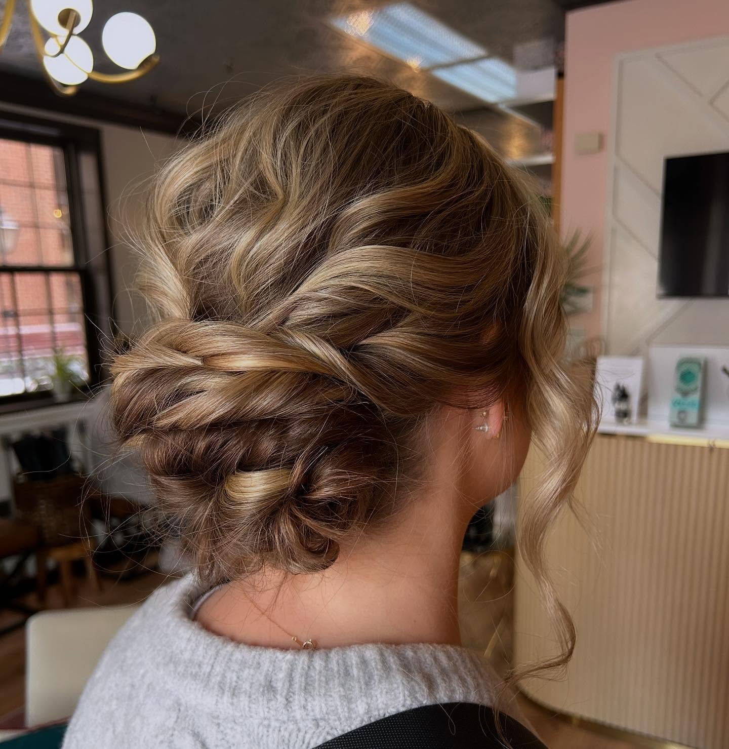 A person with blonde, wavy hair styled in a low, twisted updo, shown from the back in a modern indoor setting. | Envy Studio, Lancaster, PA