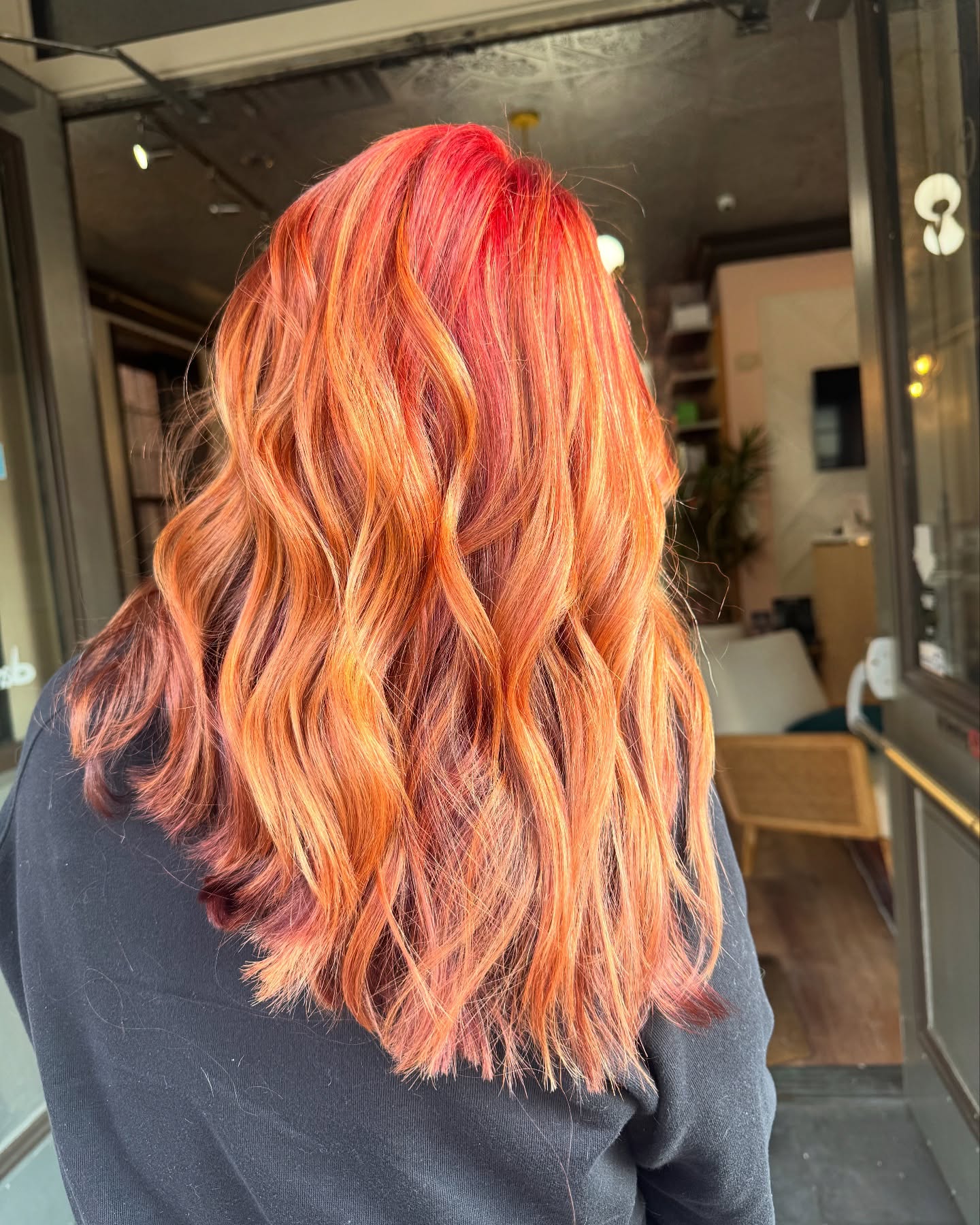 Person with long, wavy hair dyed in vibrant shades of red, orange, and copper, standing indoors with their back to the camera. | Envy Studio, Lancaster, PA