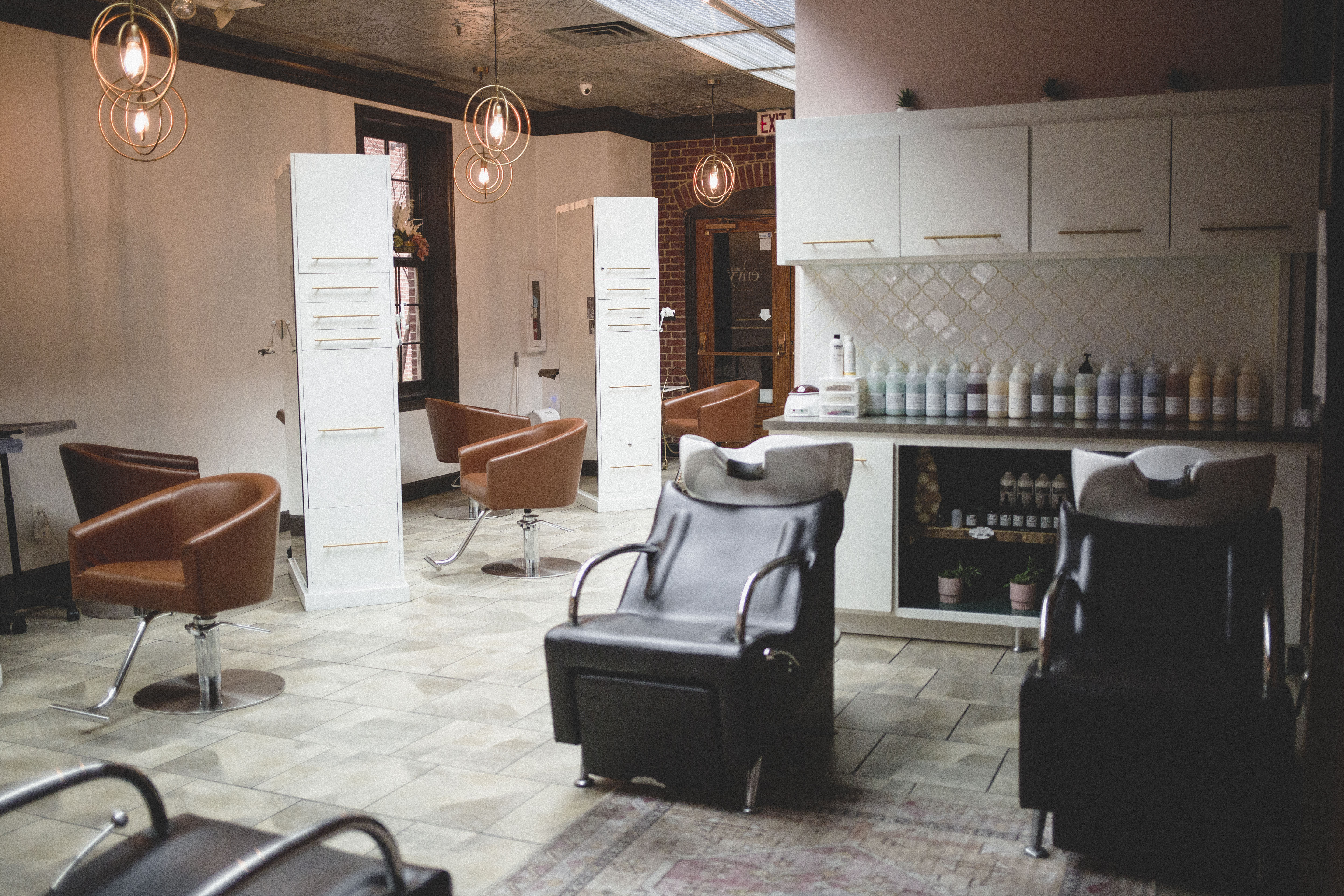 Modern hair salon interior with brown styling chairs, two black wash stations, and shelves stocked with hair products, illuminated by pendant lights. | Envy Studio, Lancaster, PA