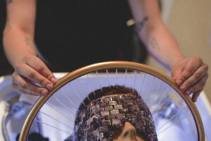 Person holding a circular frame above a face covered with a textured, stone-like mask, with hands visible on either side. | Envy Studio, Lancaster, PA