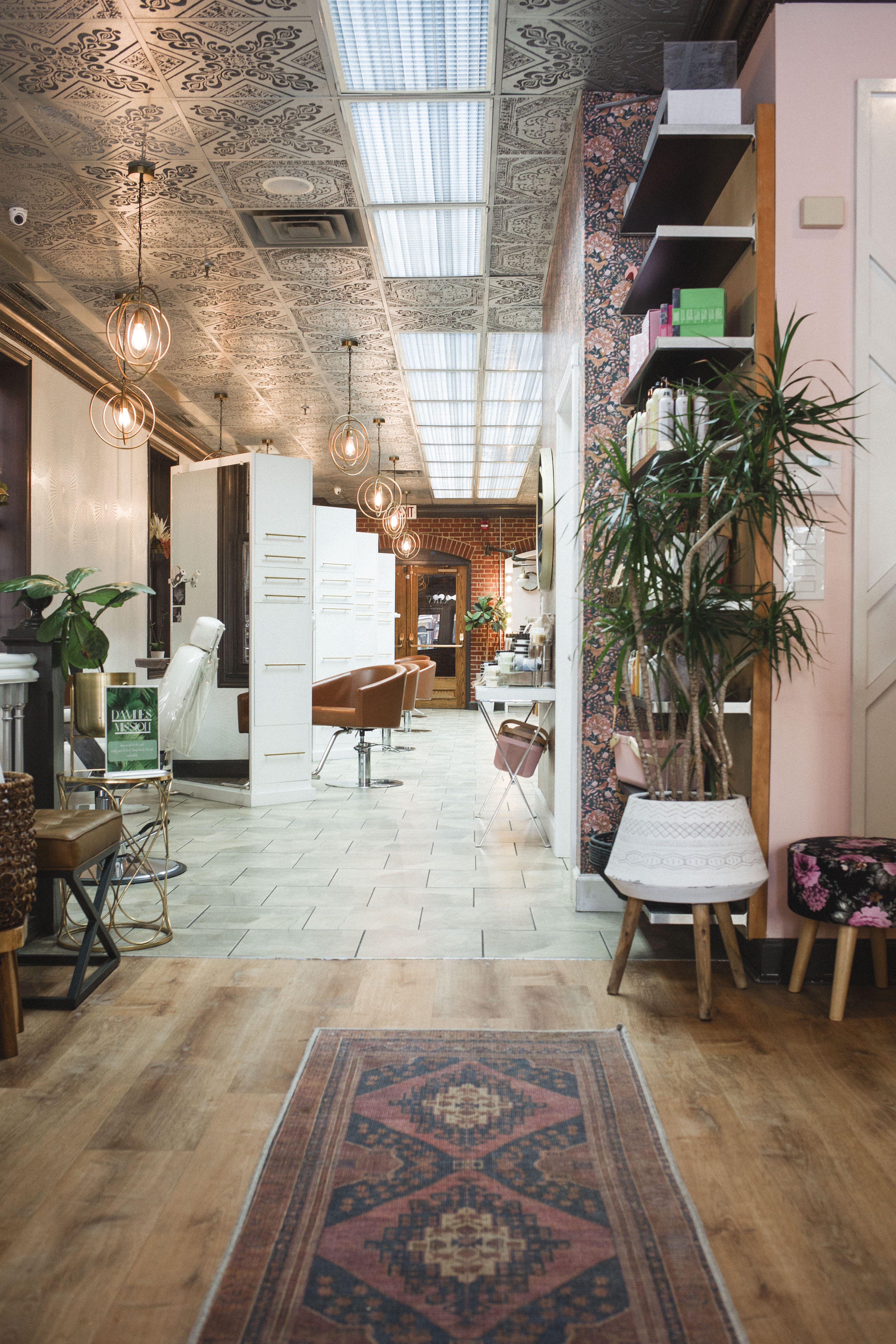 A modern salon interior with patterned tile ceiling, hanging lights, salon chairs, plants, and decorative accents along a tiled and wooden floor. | Envy Studio, Lancaster, PA