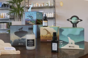 Several Davines hair care products and illustrated boxes with animal designs are displayed on a table at Envy Studio Lancaster PA, with shelves of additional products in the background. | Envy Studio, Lancaster, PA