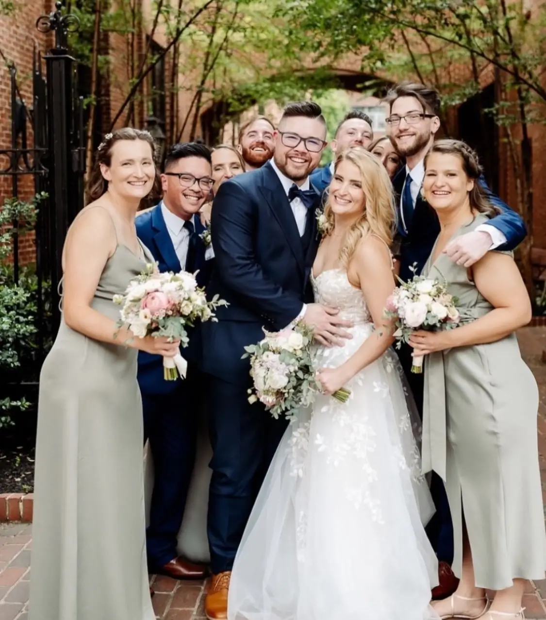 A bride and groom pose with their bridesmaids and groomsmen outdoors, all smiling and dressed in formal attire. | Envy Studio, Lancaster, PA