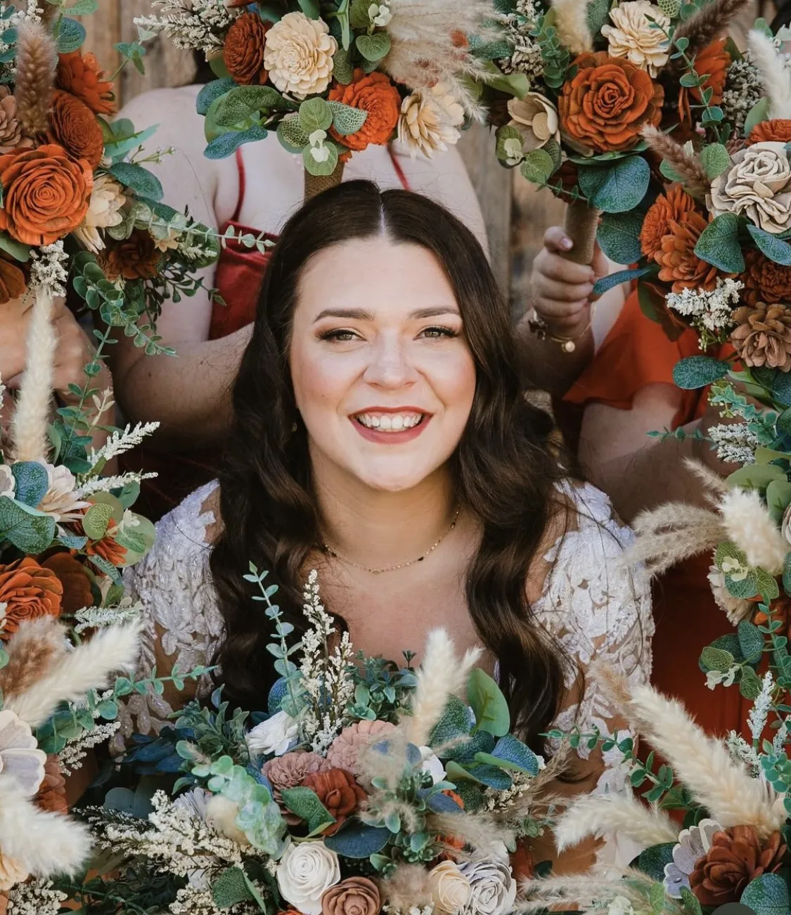 A woman with long dark hair and a white lace dress smiles, surrounded by colorful floral arrangements and other people in the background. | Envy Studio, Lancaster, PA
